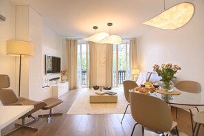 Un salon moderne doté d’un téléviseur à écran plat, d’un canapé, d’une table à manger avec des chaises et d’une grande fenêtre avec des rideaux.