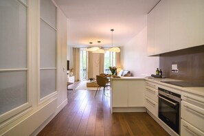A modern kitchen with white cabinetry, a built-in oven, and a dining area with a chair and table. - Le Balcon de Notre Dame (Paris)