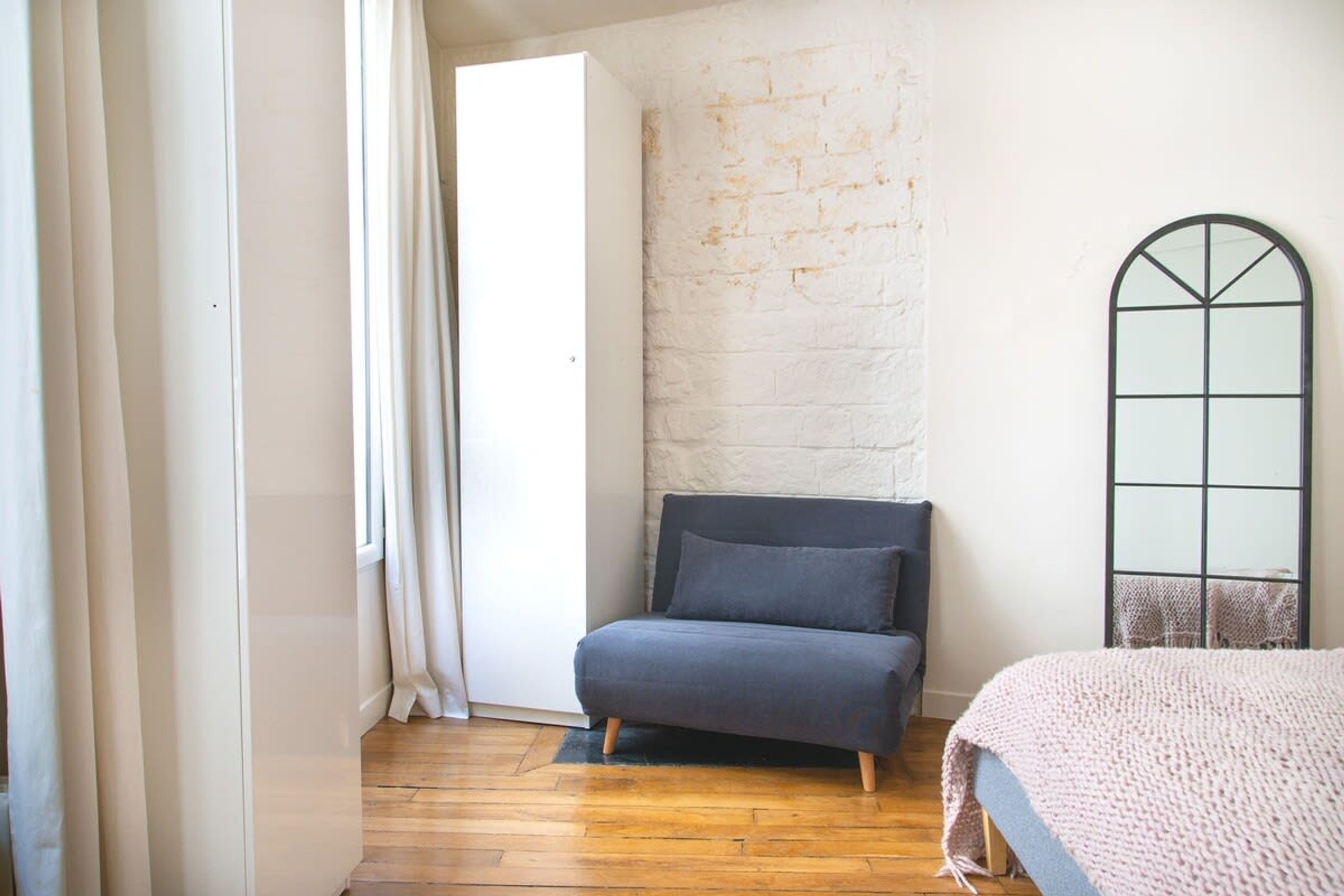 Una habitación con un sofá gris, una pared de ladrillo blanco, suelo de madera y un ventanal con marco negro.