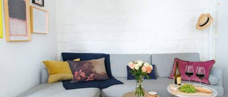 A modern living room with a grey sectional sofa, a round coffee table, and a small side table with a bottle and glasses.