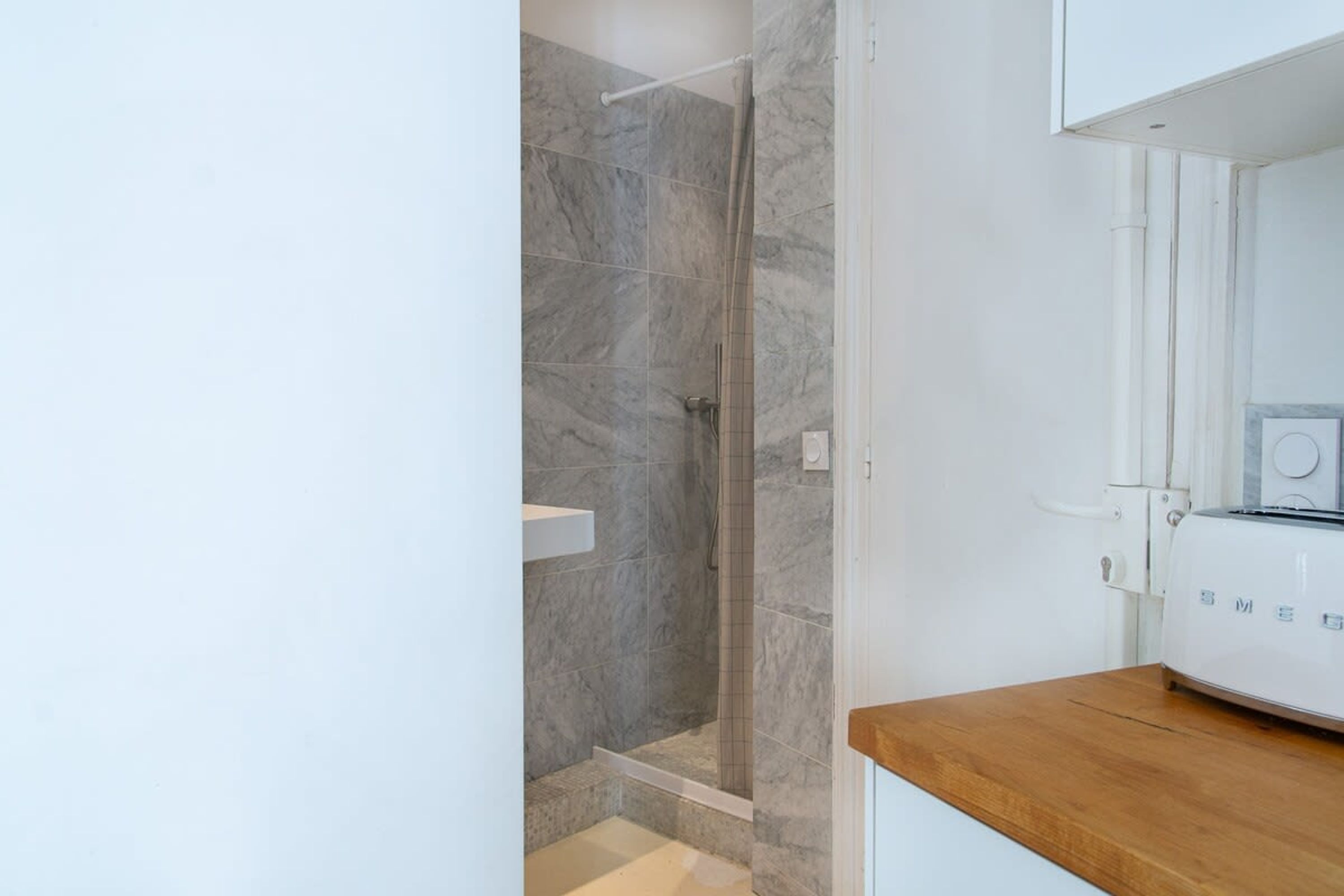 A modern bathroom with a shower, a white sink, and a wooden countertop.