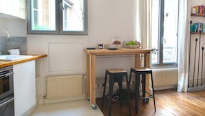 A modern kitchen with a wooden table, two stools, a radiator, and a window with curtains. - Le Plaisir du Pantheon (Paris)