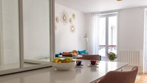 Una cocina moderna con una encimera blanca, un bol de fruta y una zona de comedor con una mesa y sillas.