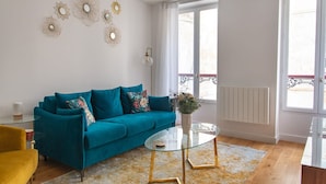 Una sala de estar moderna con un sofá color turquesa, una mesa de centro de vidrio y decoración en la pared.