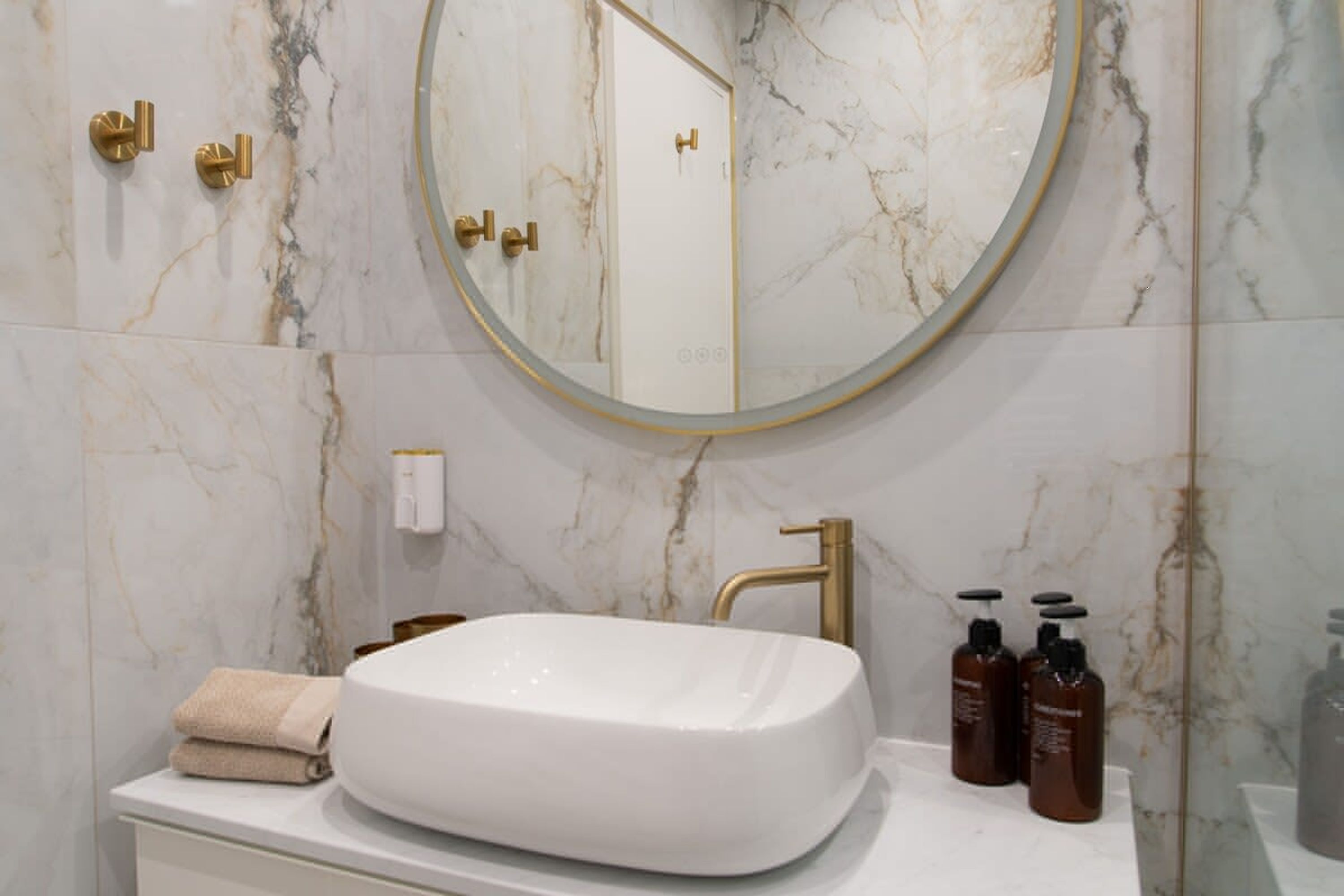 A bathroom with a white sink, gold fixtures, and a marble wall.