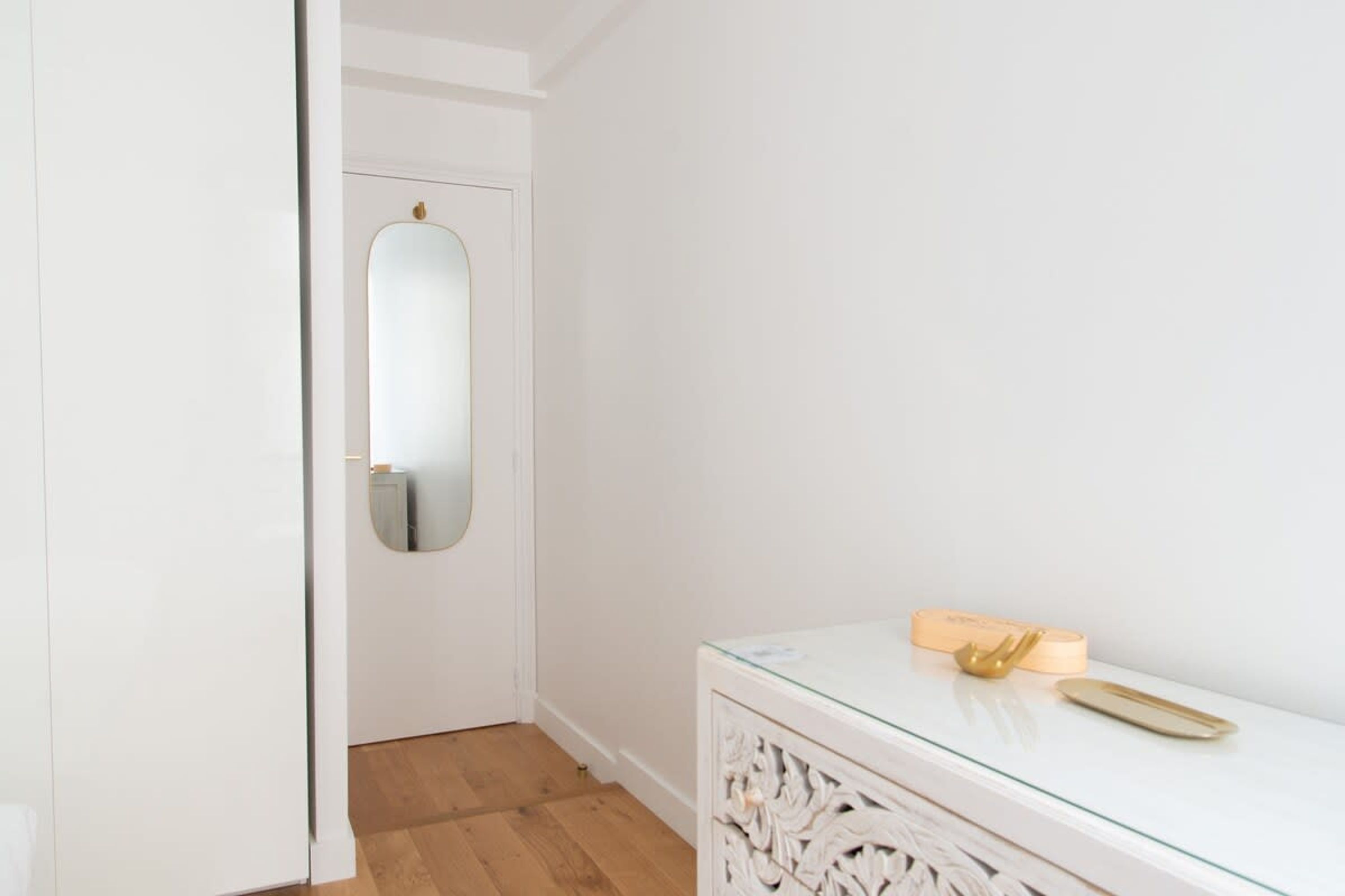 A hallway with a white door, a mirror, and a glass cabinet with decorative items.