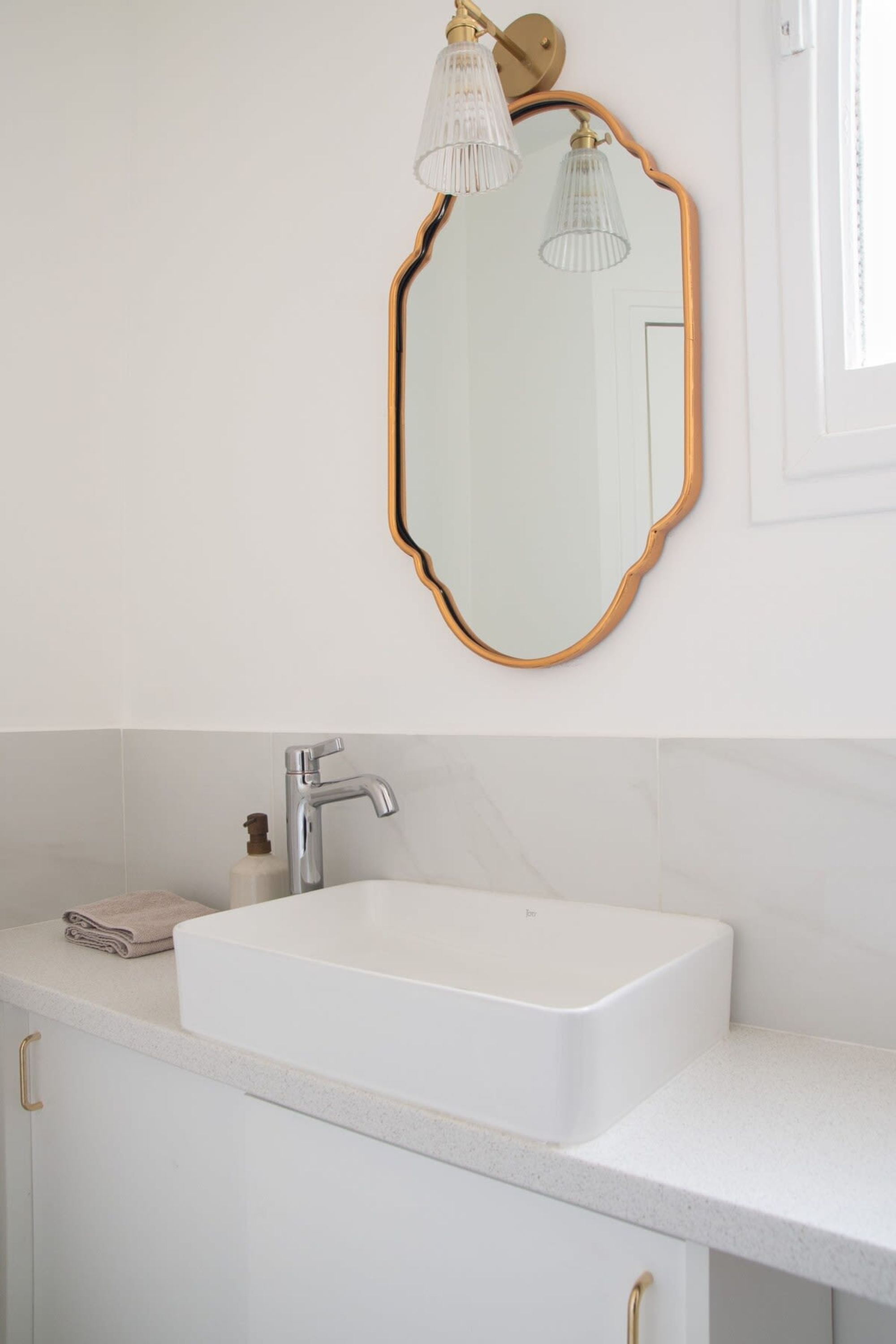 Une salle de bain avec un lavabo blanc, un miroir à cadre doré et un luminaire placé au-dessus.