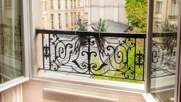 A balcony with a wrought iron railing, a radiator, and a view of Parisian buildings. - Studio en Isle - Monthly Rental (Paris)