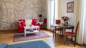 A living room with a stone wall, red furniture, a white coffee table, and a dining area with a wooden table and chairs. - Studio en Isle - Monthly Rental (Paris)