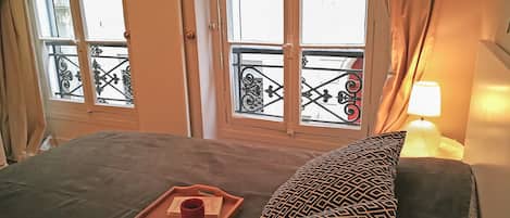 A bed with a tray of pastries and a cup, a patterned pillow, and a lamp.