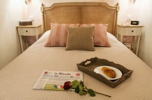 Un lit bien fait, avec un oreiller à rayures, un plateau contenant un croissant, une rose et un journal.