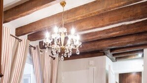 A dining area with a round table, four chairs, a chandelier, and wooden beams on the ceiling. - Le Merlot du Marais - Pompidou (Paris)