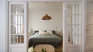 A bedroom with a bed, a hanging light fixture, and a wicker chair.