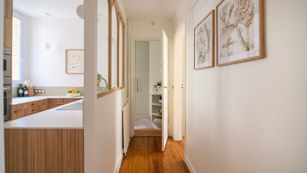 A narrow hallway with wooden flooring, white walls, and a kitchen area on the left. There are framed artworks on the right wall. - Deco St Antoine in Paris (Paris)