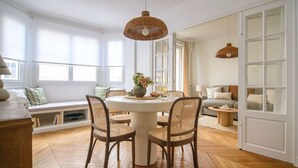 A dining area with a round table, wicker chairs, and a hanging light fixture.