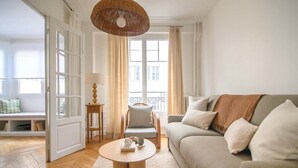 A living room with a sofa, a round coffee table, a wicker lamp, and a view of the outside through large windows.