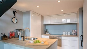 Une cuisine moderne avec des meubles blancs, un évier en acier inoxydable et un plan de travail en bois.