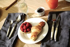 A plate with a croissant and a bowl of strawberries, a glass of water, and a cup of tea on a wooden table. - Loft Saint Germain - Bon March (Paris)