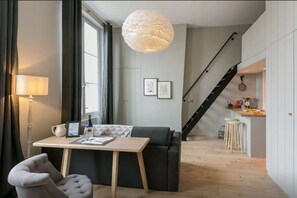 A modern living room with a sofa, a table, and a lamp. There is a staircase leading to a kitchen area. - Loft Saint Germain - Bon March (Paris)