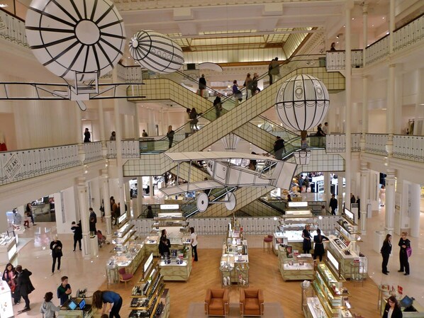A multi-level shopping mall with escalators and a central atrium. - Loft Saint Germain - Bon March (Paris)