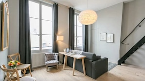 Un salon moderne avec un canapé gris, une table basse en bois, un fauteuil gris et une grande fenêtre avec des rideaux.