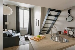 A modern kitchen with a built-in sink, a wooden countertop, and a dining area with a sofa and a lamp. - Loft Saint Germain - Bon March (Paris)