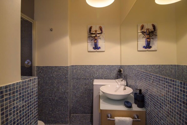 A bathroom with a white sink, blue tiled walls, and two lobster artwork pieces on the wall. - Le Marais Moderne in Paris (Paris)