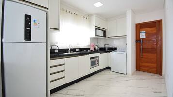 A modern kitchen with white cabinets, a black countertop, a built-in microwave, a stainless steel sink, and a wooden door.