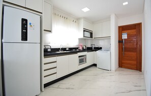 A modern kitchen with white cabinets, a black countertop, a built-in microwave, a stainless steel sink, and a wooden door. - Residencial Fiametti-Praia dos Ingleses (Florianopolis)