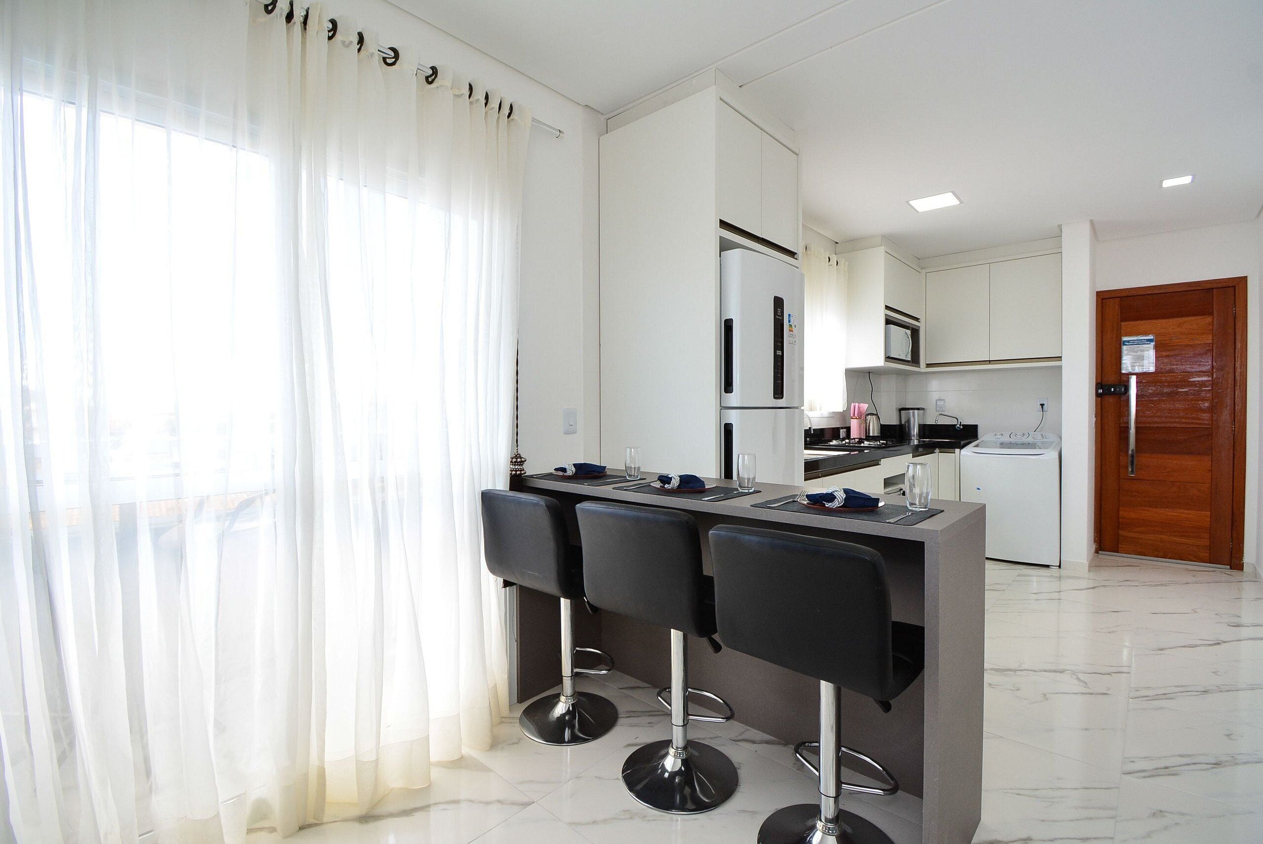 A modern kitchen with a bar area, white cabinets, and a wooden door.