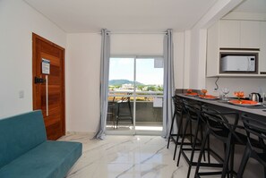 A modern kitchen with a built-in microwave, a dining area with bar stools, and a sliding glass door leading to a balcony with a view of the city.