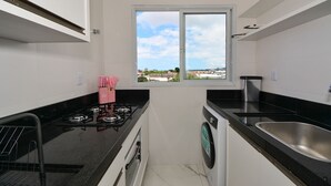 Une cuisine compacte équipée d’une cuisinière à gaz, d’un lave-linge, d’un évier et d’une fenêtre donnant sur la ville.
