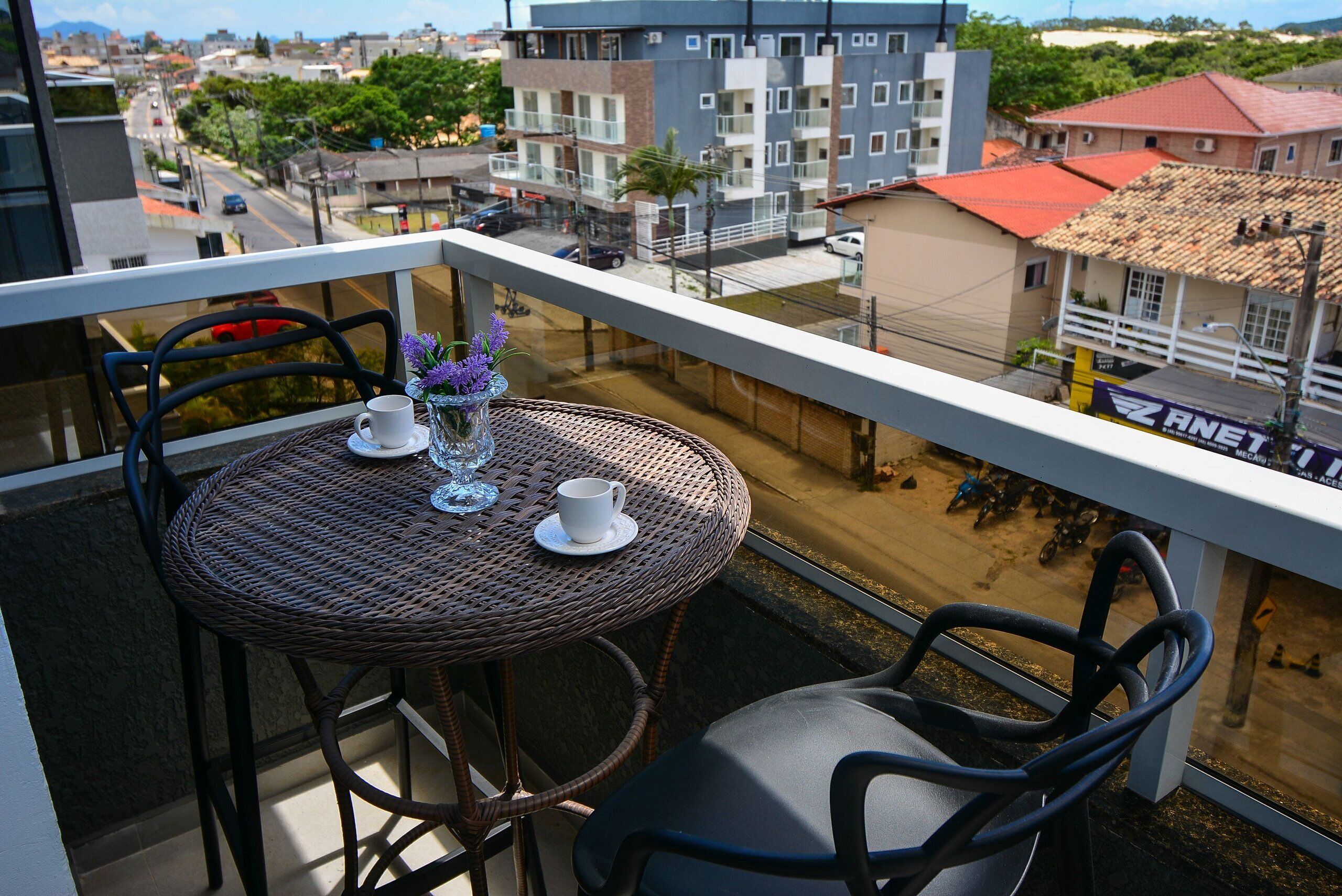 A balcony with wicker furniture, a white cup, and a vase with purple flowers.