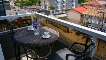 A balcony with wicker furniture, a white cup, and a vase with purple flowers.