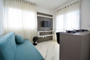 Un salon moderne comprenant un canapé, un téléviseur fixé au mur, une table à manger avec des chaises et un ventilateur.