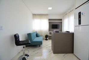 A modern living room with a sofa, a bar area, a flat-screen TV, and a refrigerator. - Residencial Fiametti-Praia dos Ingleses (Florianopolis)