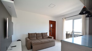 Un salon moderne avec un canapé, un téléviseur à écran plat, une table avec un plateau en verre et un balcon offrant une vue agréable.