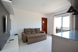 Una sala moderna con sofá, televisor de pantalla plana, mesa de vidrio y balcón con vistas.
