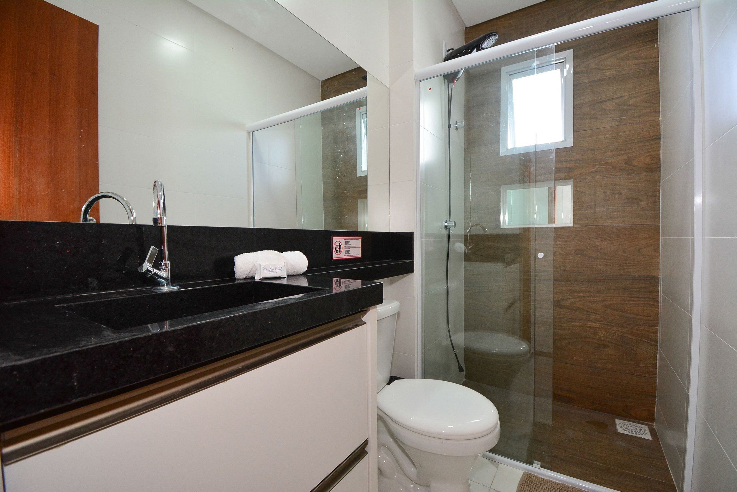 A modern bathroom with a black countertop, a white toilet, and a glass-enclosed shower.