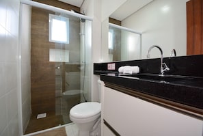 A bathroom with a glass-enclosed shower, a white toilet, a black countertop, and a mirror.