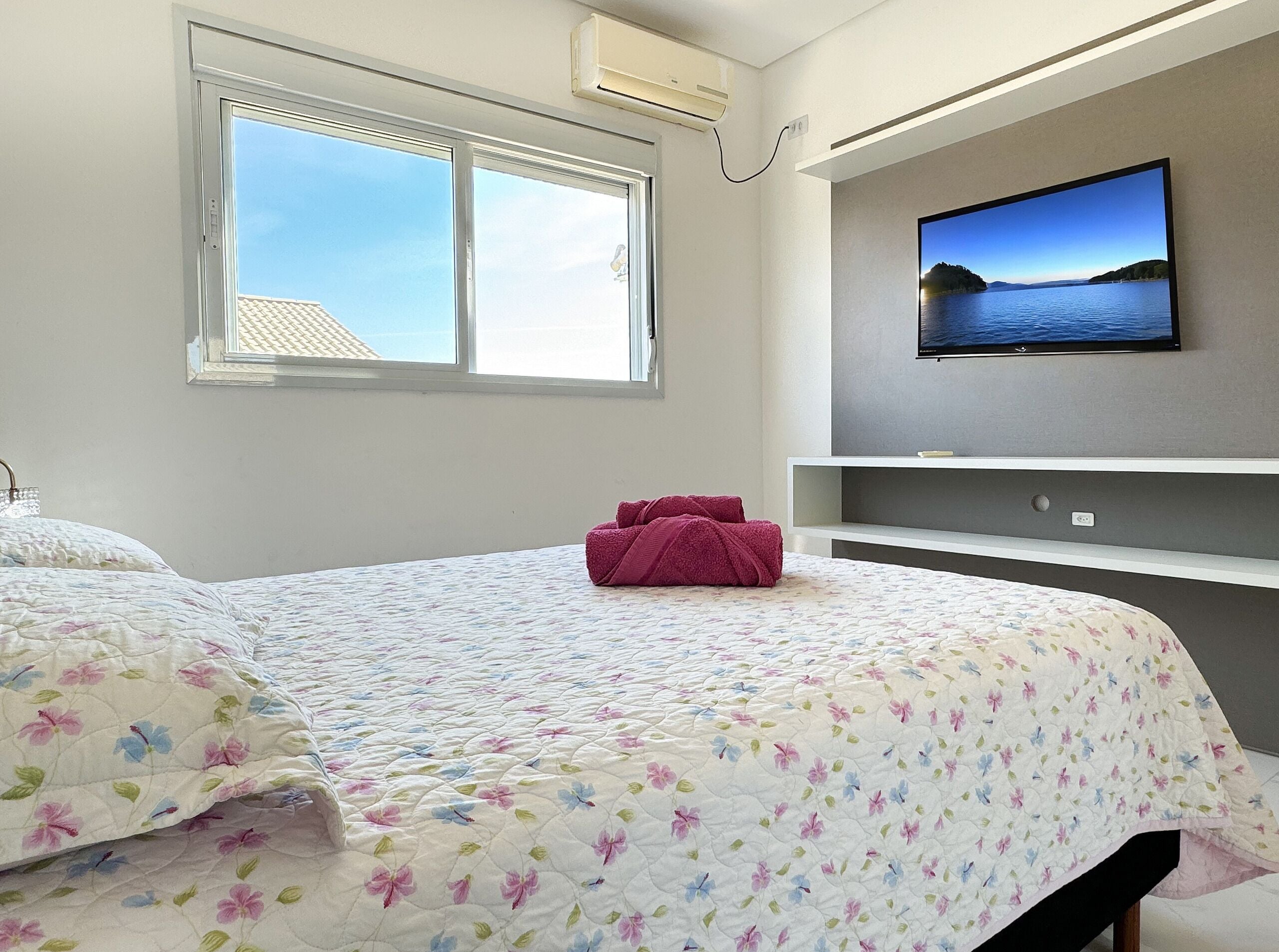 A bedroom with a bed, a window, a TV on the wall, and a shelf.