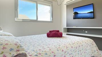 A bedroom with a bed, a window, a TV on the wall, and a shelf.