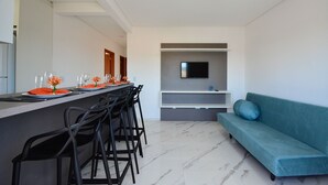 Ein modernes Wohnzimmer mit einer Couch, einem an der Wand befestigten Fernseher und einem Essbereich mit Stühlen und einem Tisch für zwei Personen.
