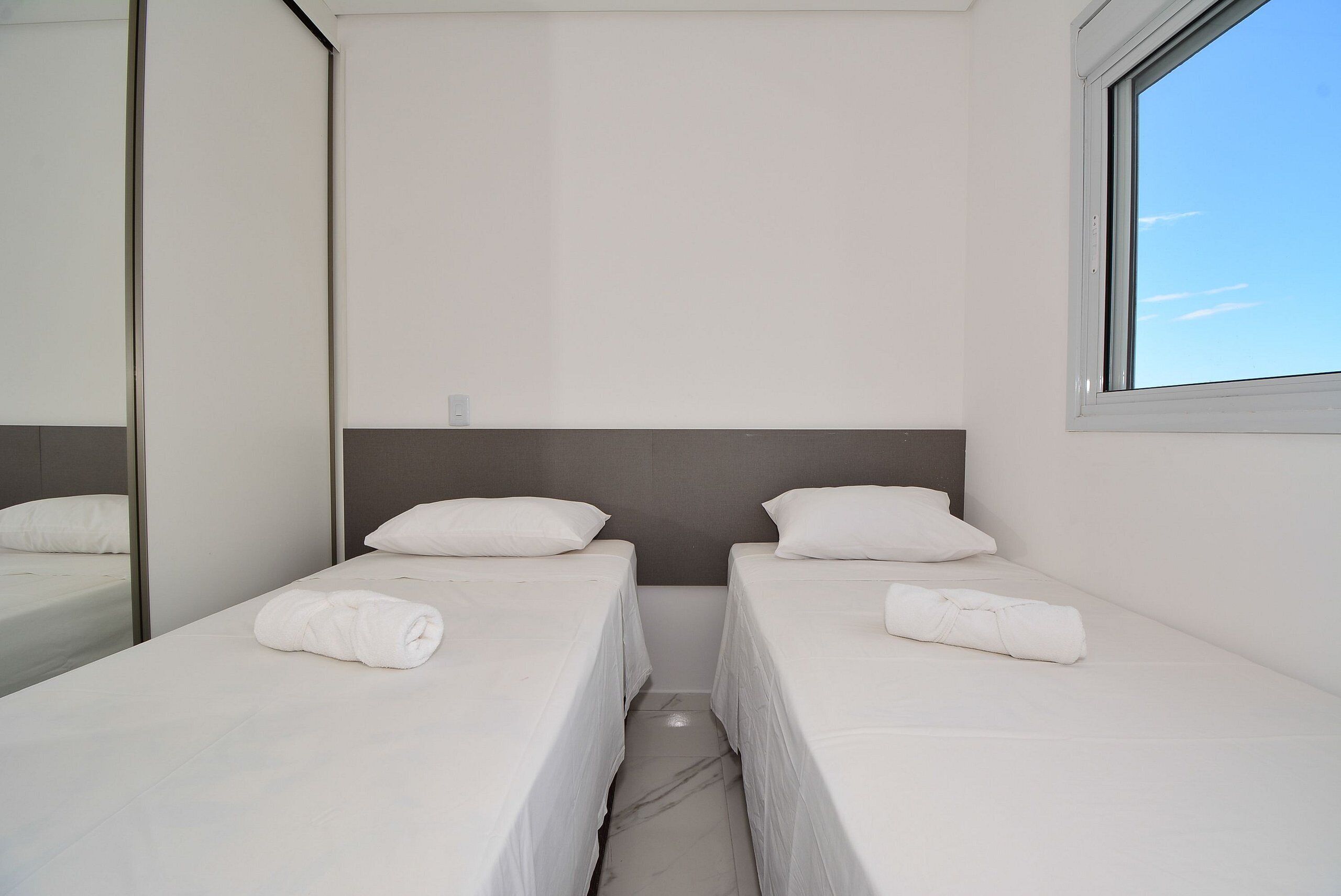 A twin room with two single beds, a large mirror, and a window.