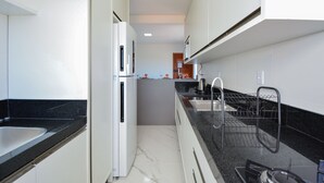 Eine schmale Küche mit einem weißen Kühlschrank, einer schwarzen Arbeitsplatte und einem Geschirrständer.