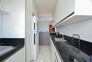 Una cocina estrecha con un refrigerador blanco, una encimera negra y un escurreplatos.