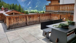 Un terrazzo in legno con vista sulle montagne, un tavolo e delle sedie.