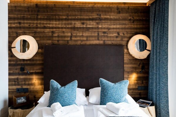 A neatly made bed with white and blue bedding, a dark headboard, and wooden wall panels. - Stay Near Ski Arena Wildkogel (Neukirchen am Grossvenediger)