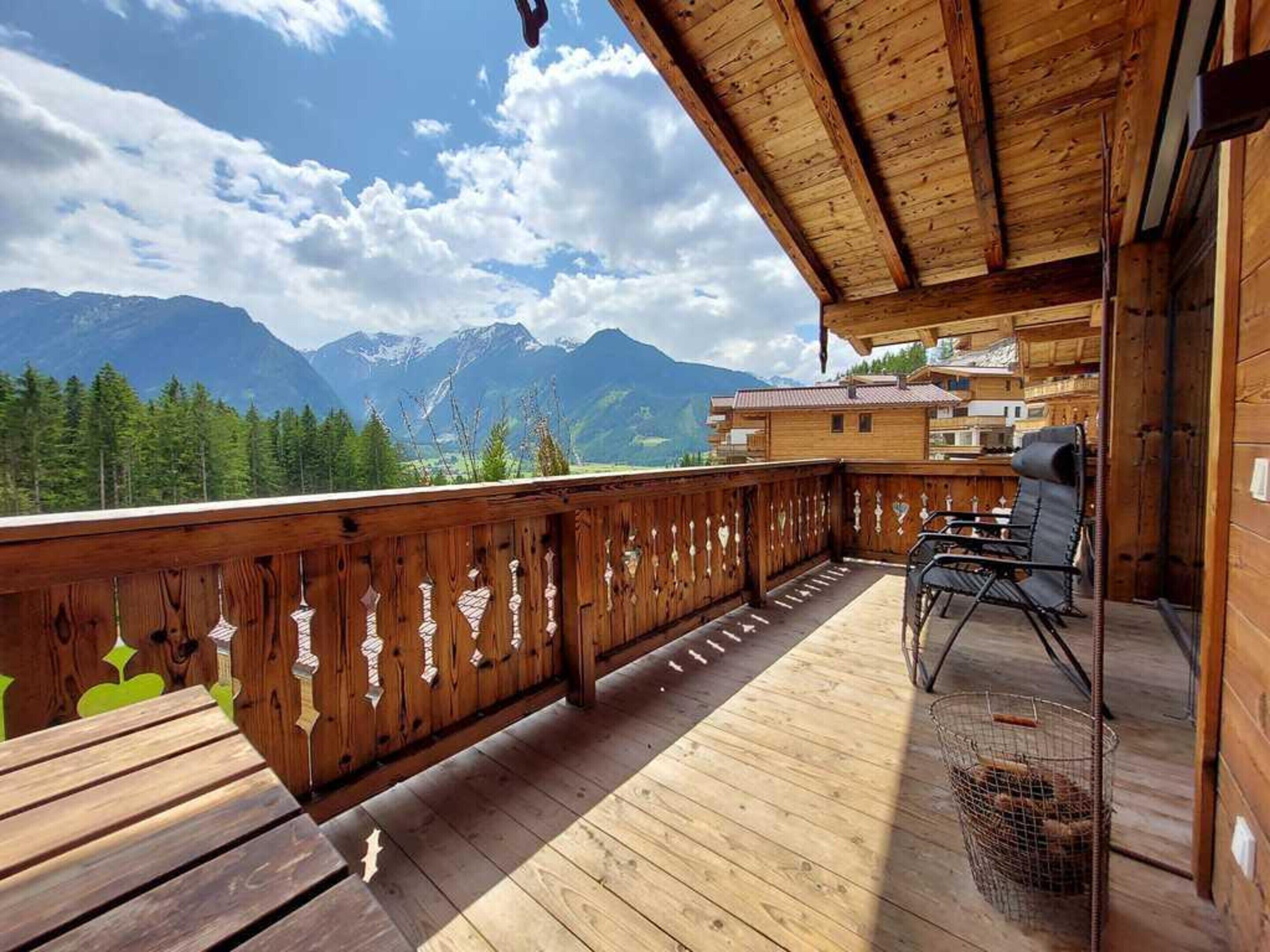 A wooden deck with a view of mountains, a chair, and a table.