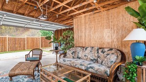 A covered patio area with a wicker sofa, a matching ottoman, and a glass coffee table. - Tiki Bar! Near wineries, Sleeping Bear Dunes, TC - Cedar Cottage (Cedar)